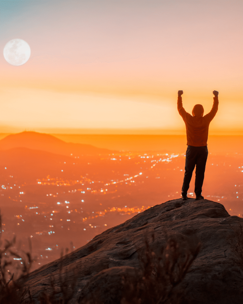 pessoa no topo da montanha com braços erguidos representando força interior e coragem